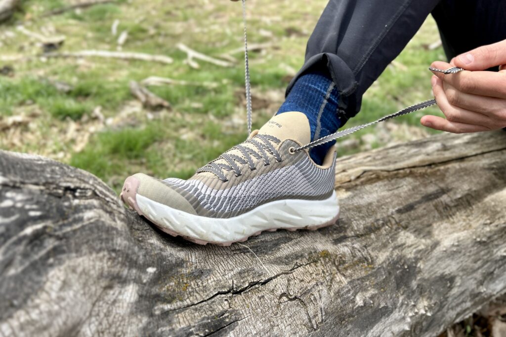 Close up image of a person tying the shoelaces on a pair of trail runners while sitting on a log.