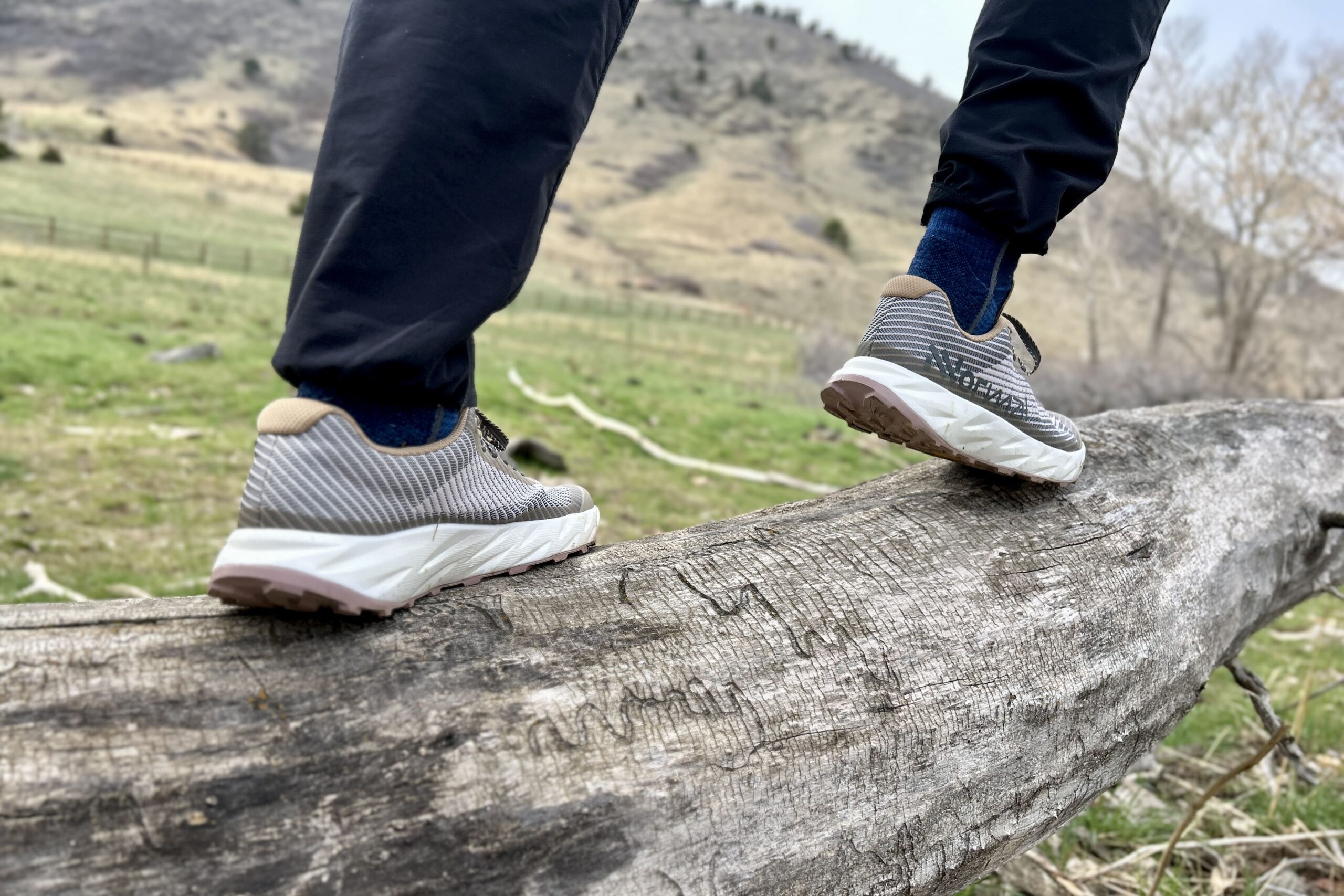 A person from the knees down walking across a log in a wilderness setting.