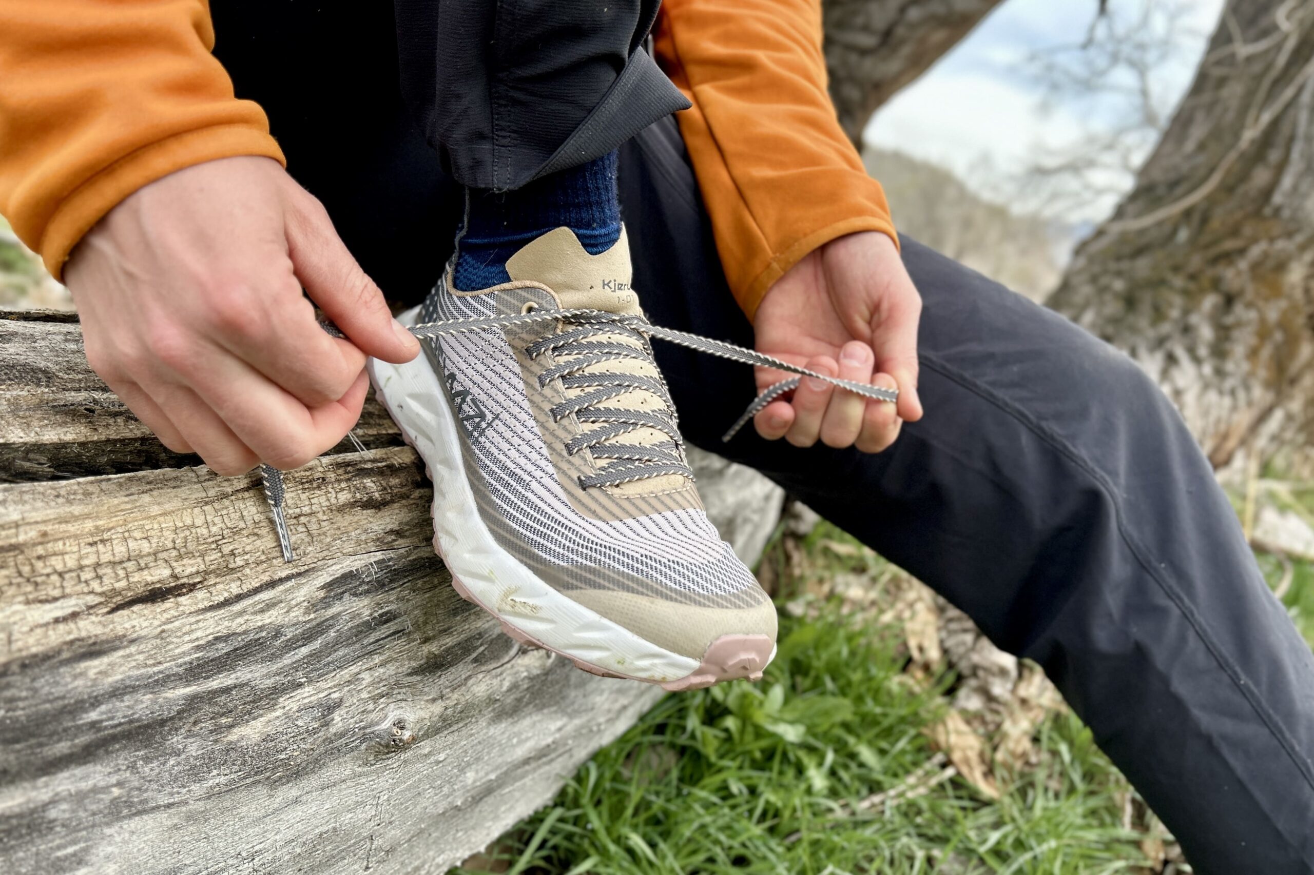 Close up of a person tying a pair of trail running shoes while sitting on a log