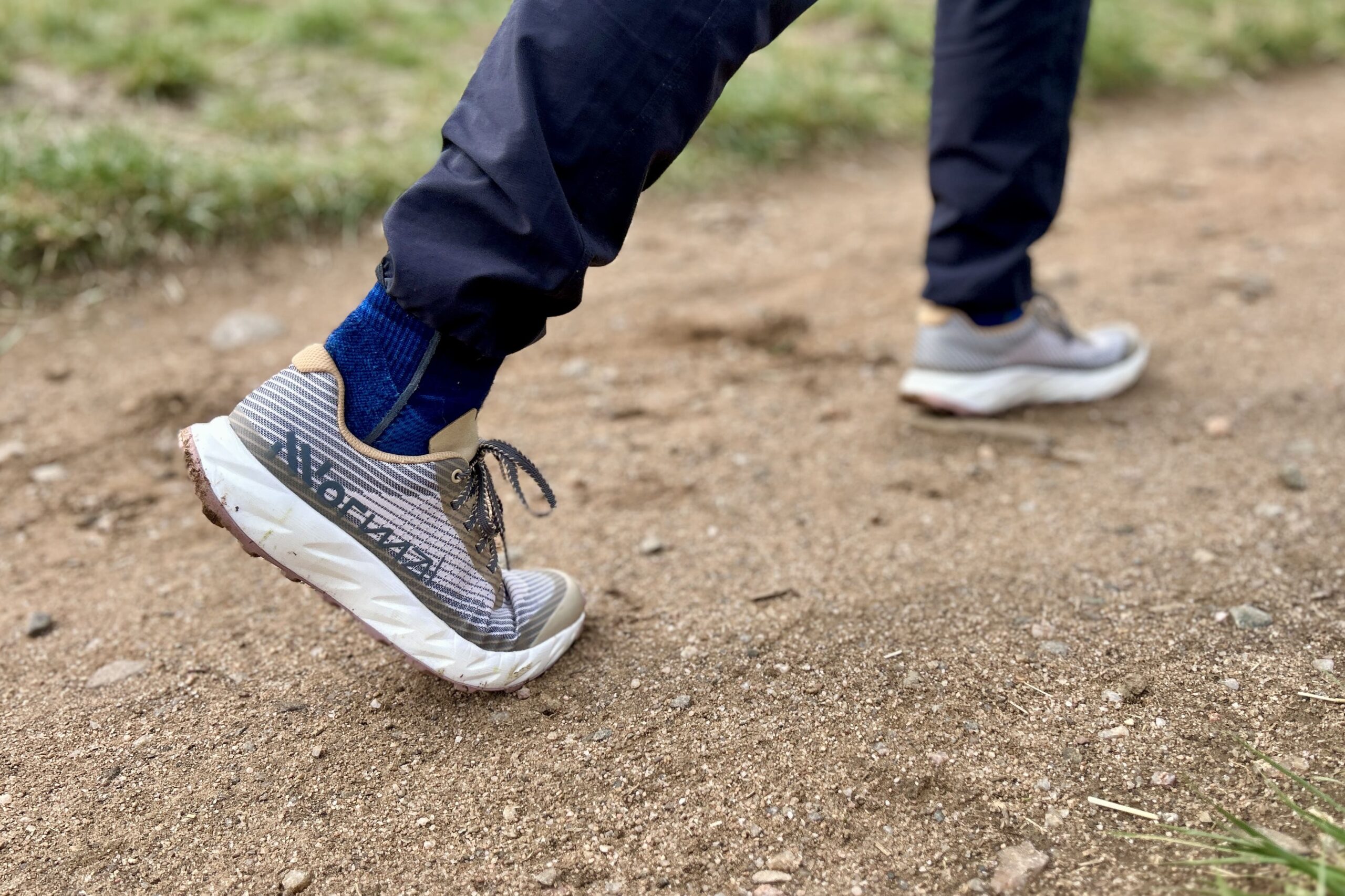 Close up from the side of a person walking in a pair of trail runners on a dirt path.