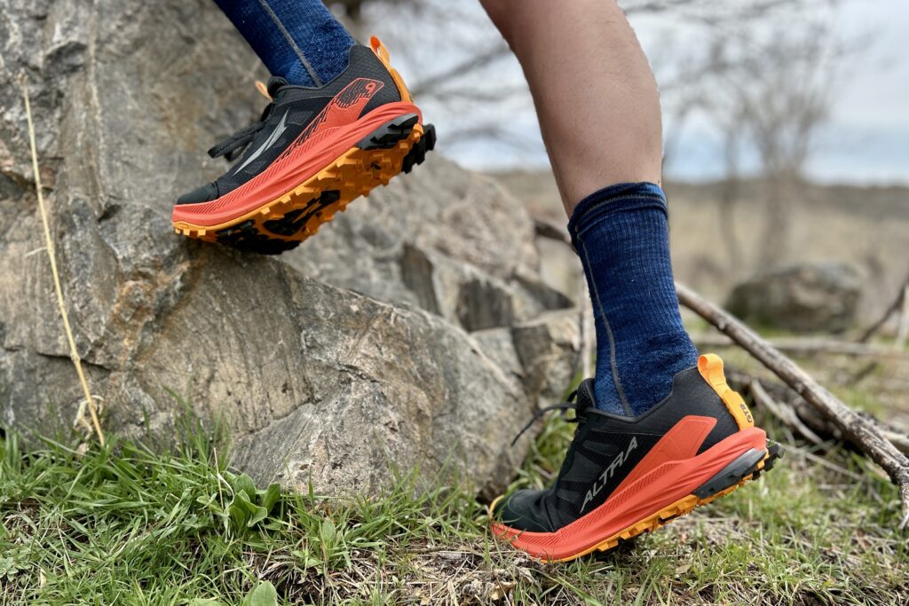A close up from knees down of a person in bright trail runners stepping up on a rock.