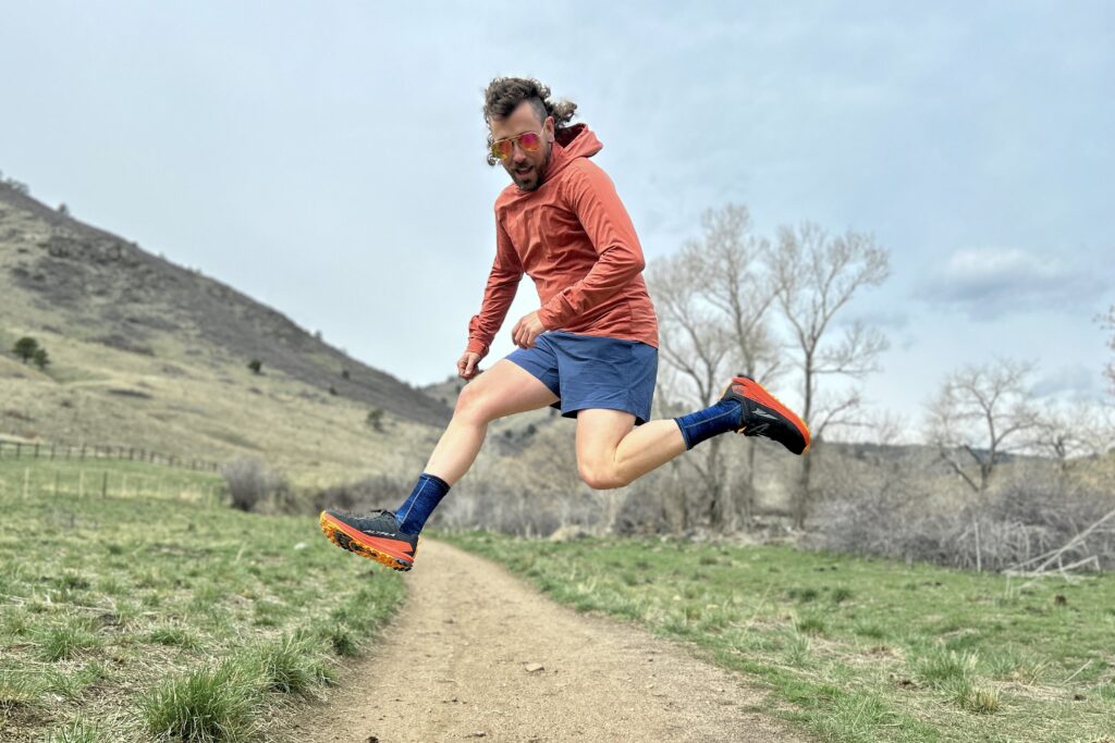 A man in running attire jumps in the air in a hilly setting.