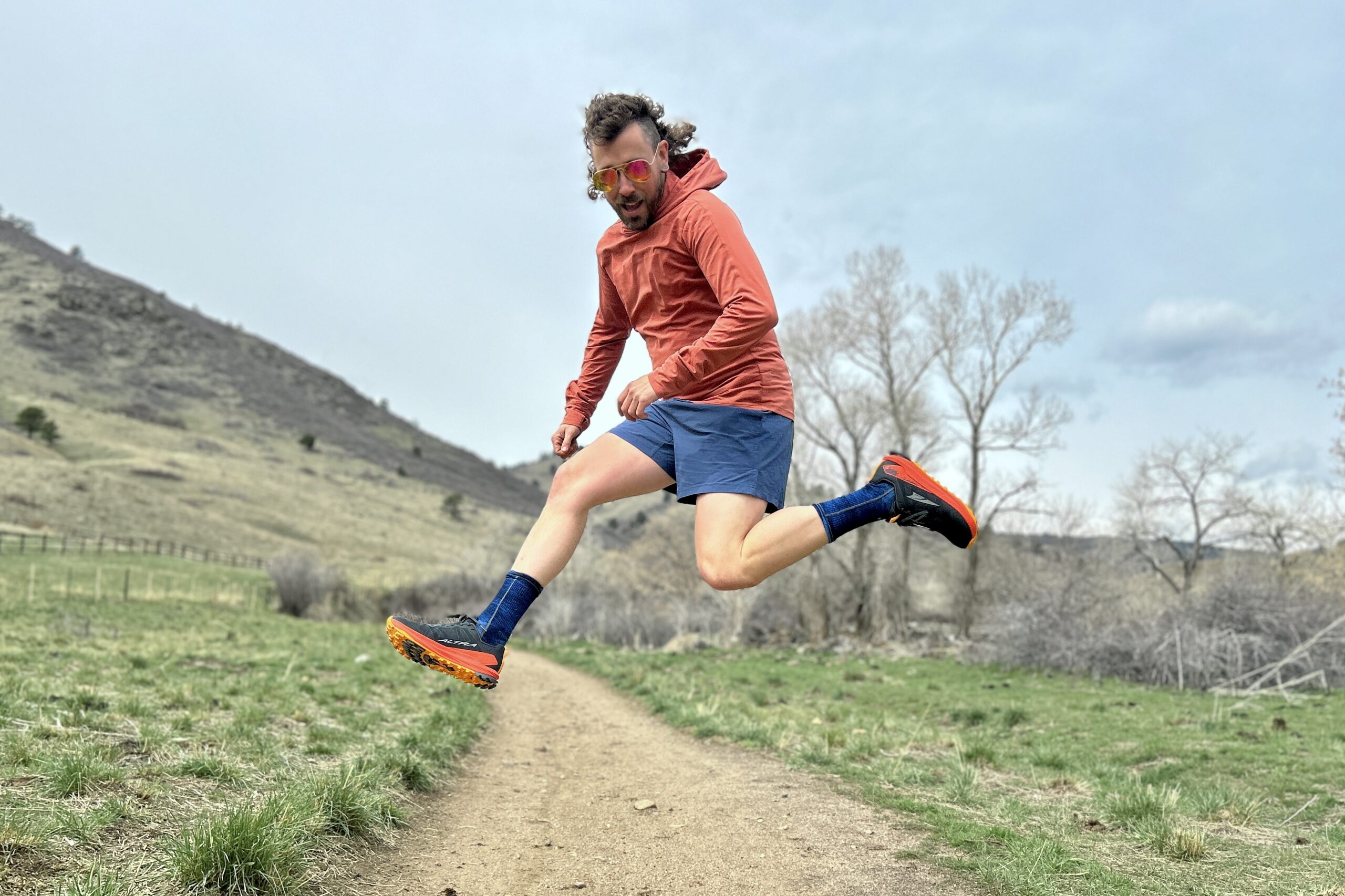 A man in running attire jumps in the air in a hilly setting.