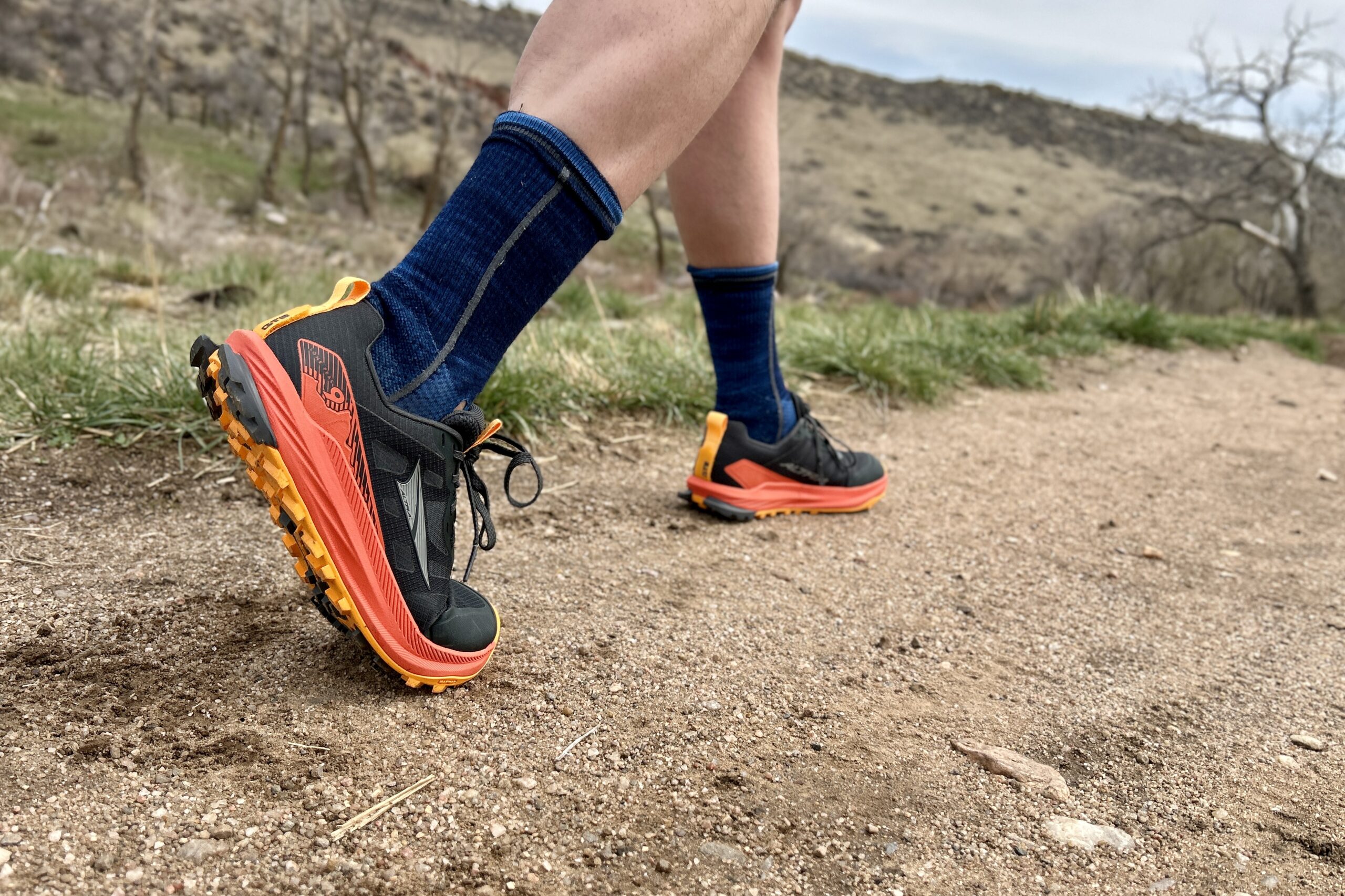 Close up from the knees down of a person walking in bright trail running shoes.
