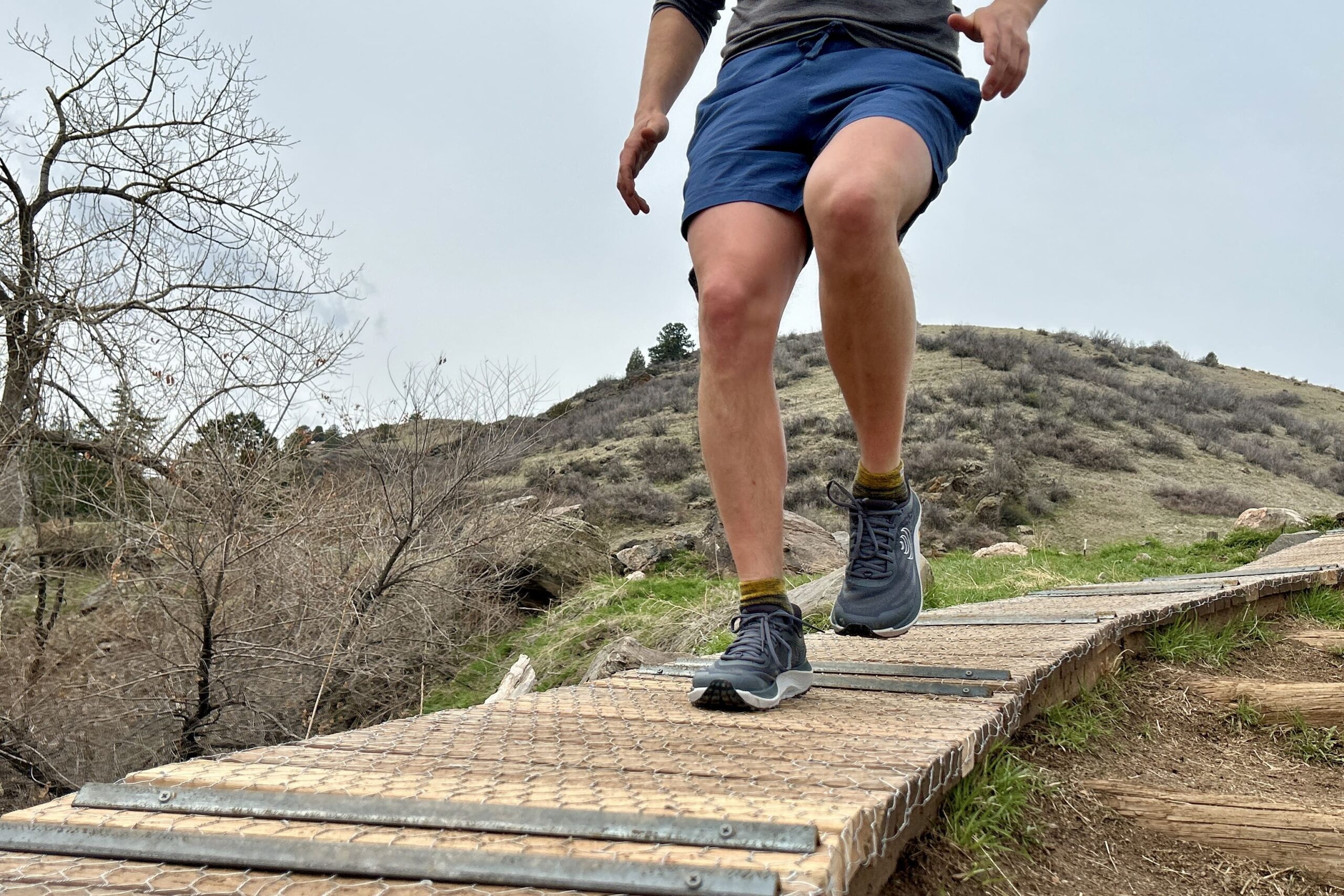 Image of a person running downhill on a wooden trail in shorts and a pair of trail runners.