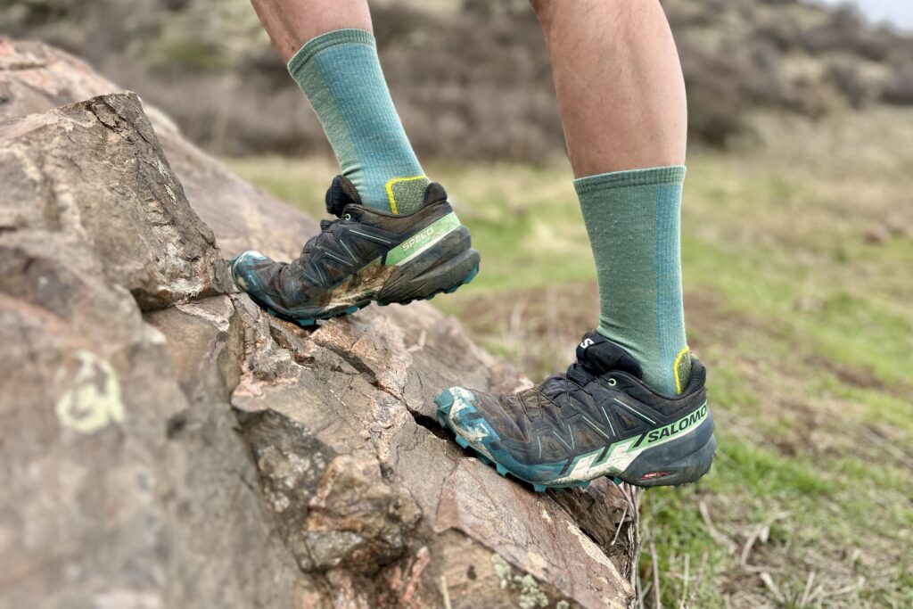 Close up from the knees down of a man climbing up a steep rock.