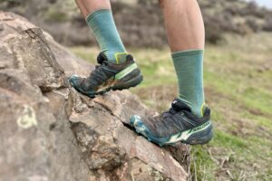 Close up from the knees down of a man climbing up a steep rock.