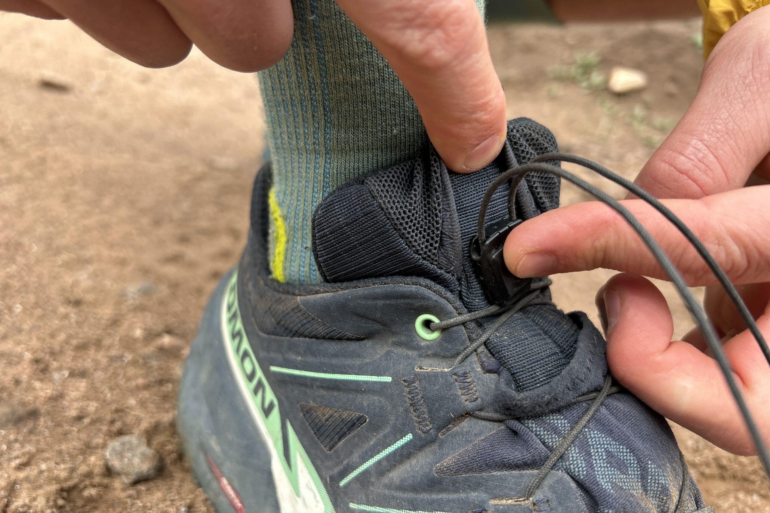 Very close up image of a person tucking a pair of laces on trail runners into a pocket on the tongue.