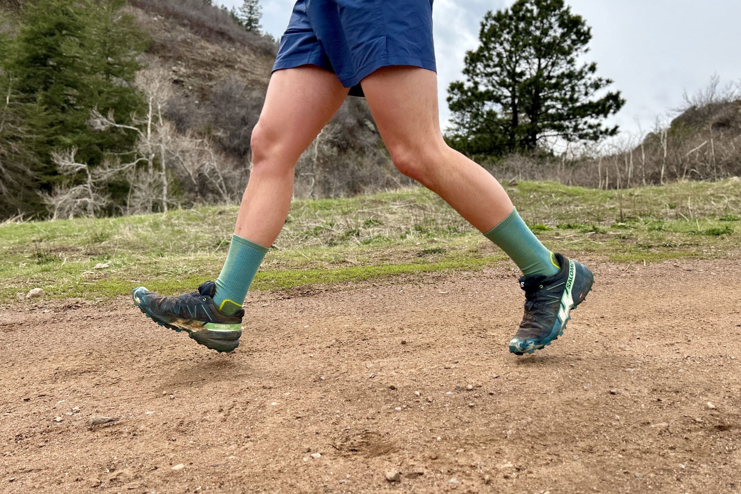 Side-view of a runner wearing shorts and trail runners as they jog down a trail