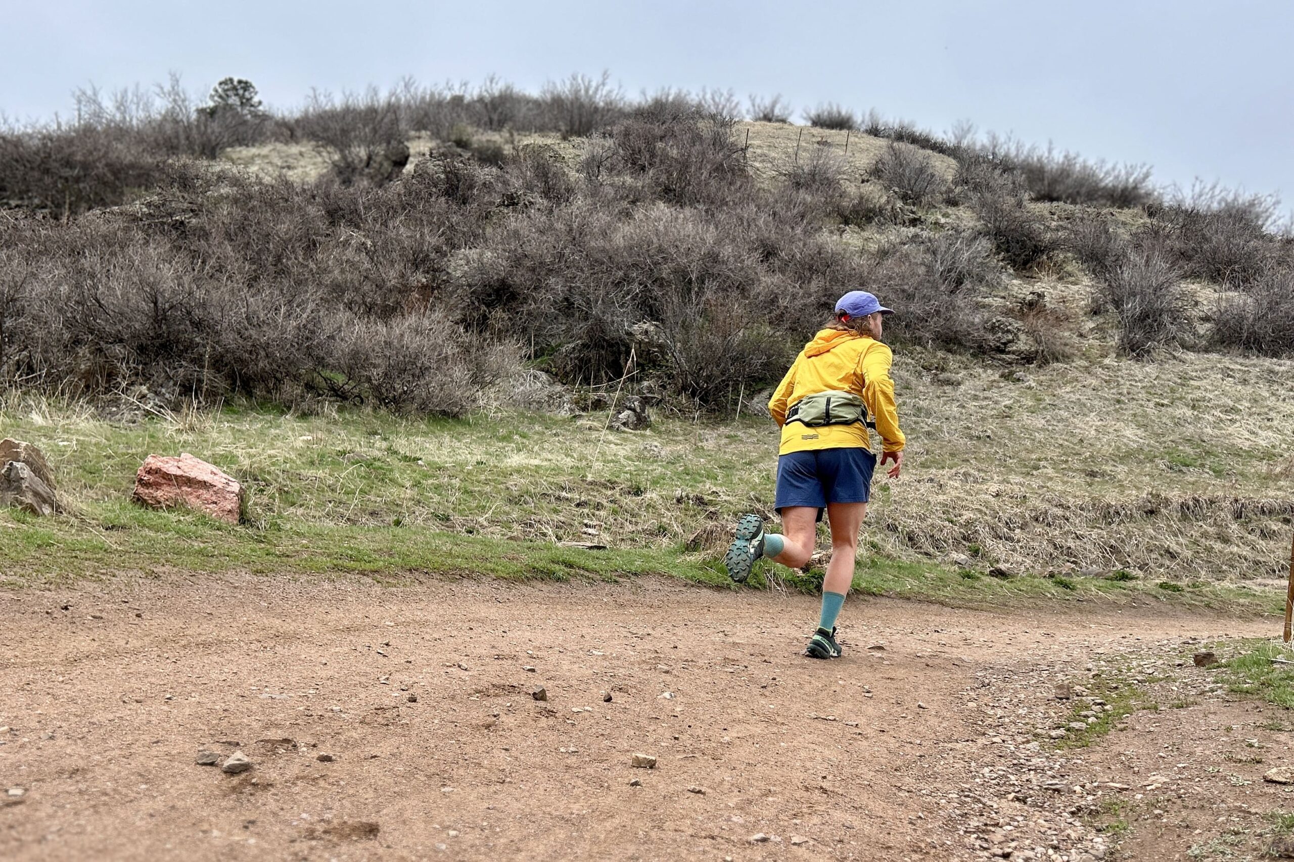 A man in a yellow jacket runs down a wide dirt trail in a wilderness setting