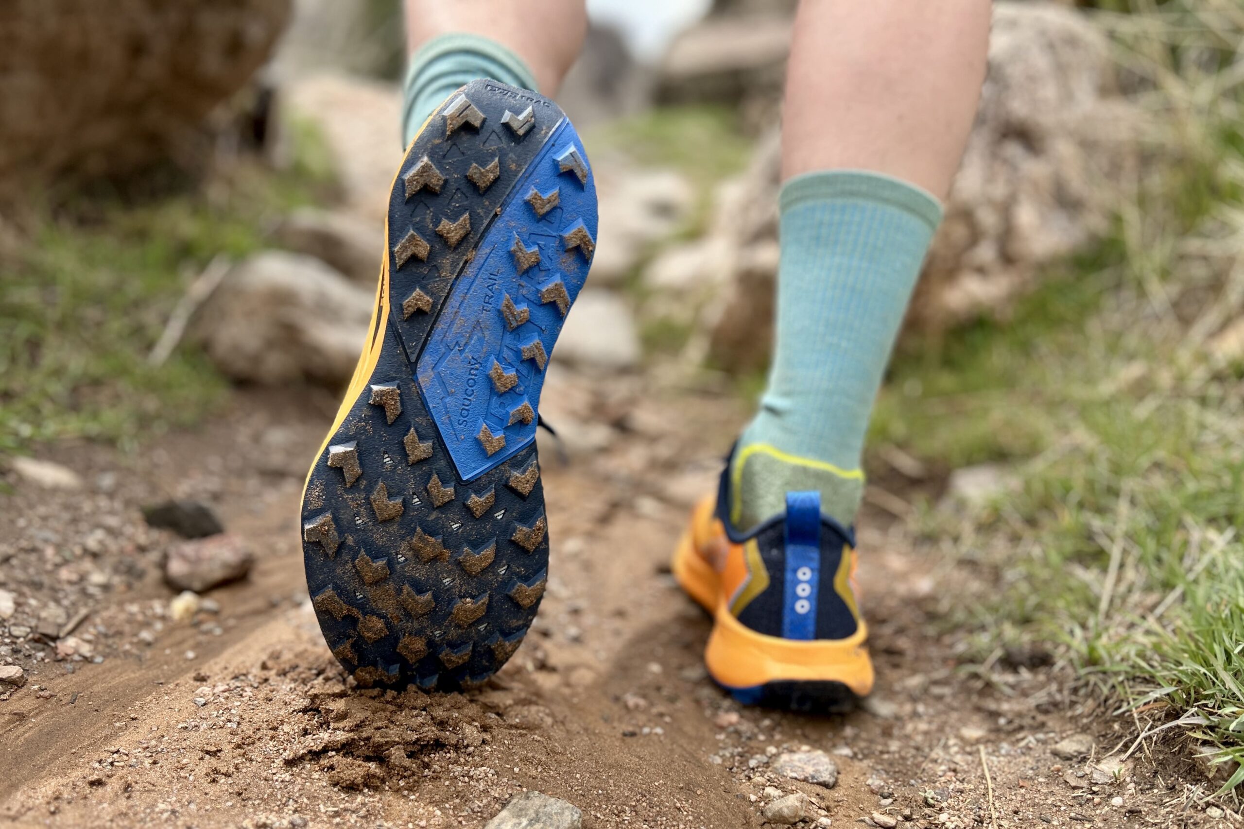 A person walks up a muddy trail. Image is zoomed in on the tread of their shoes covered in mud.