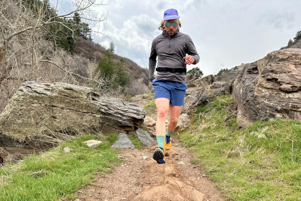 A man in running gear runs down a rocky section of trail in a mountain setting