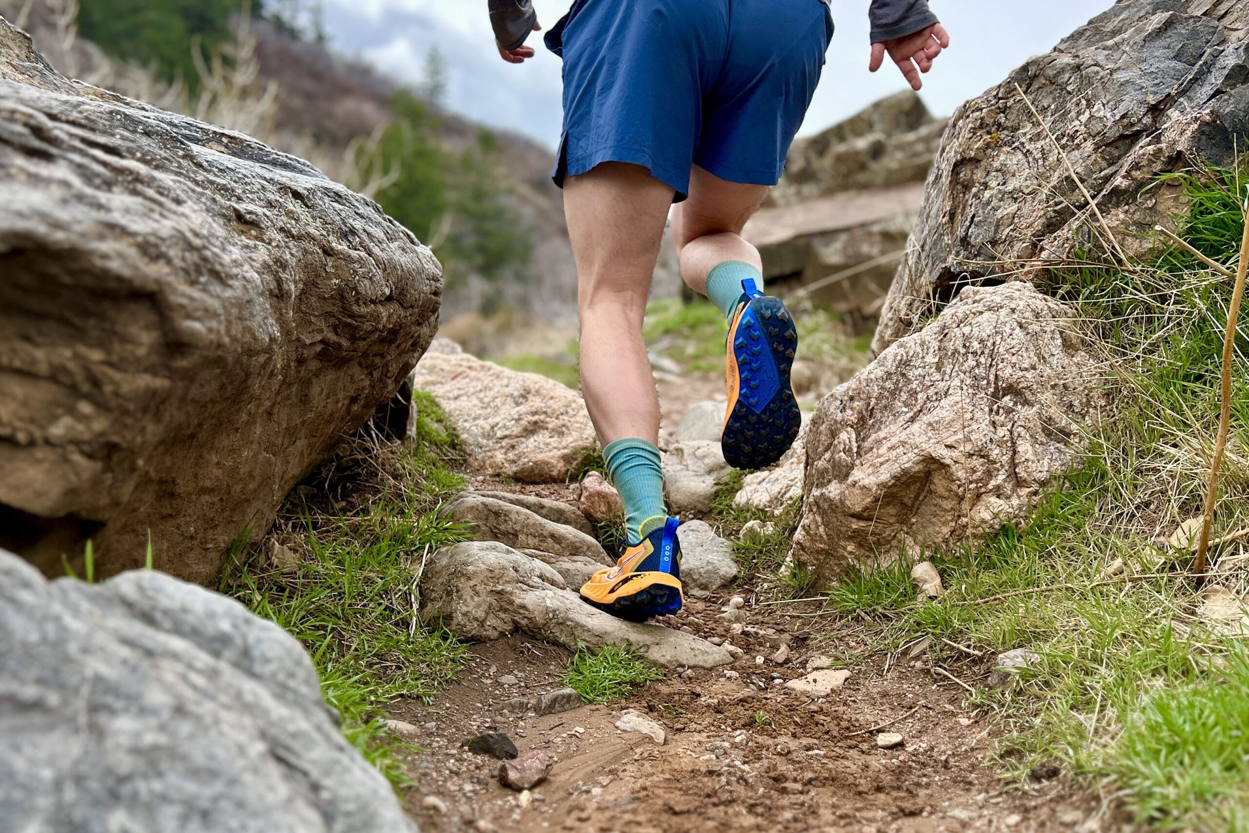 A person in sports attire from the waist down runs through a rocky section of trail.