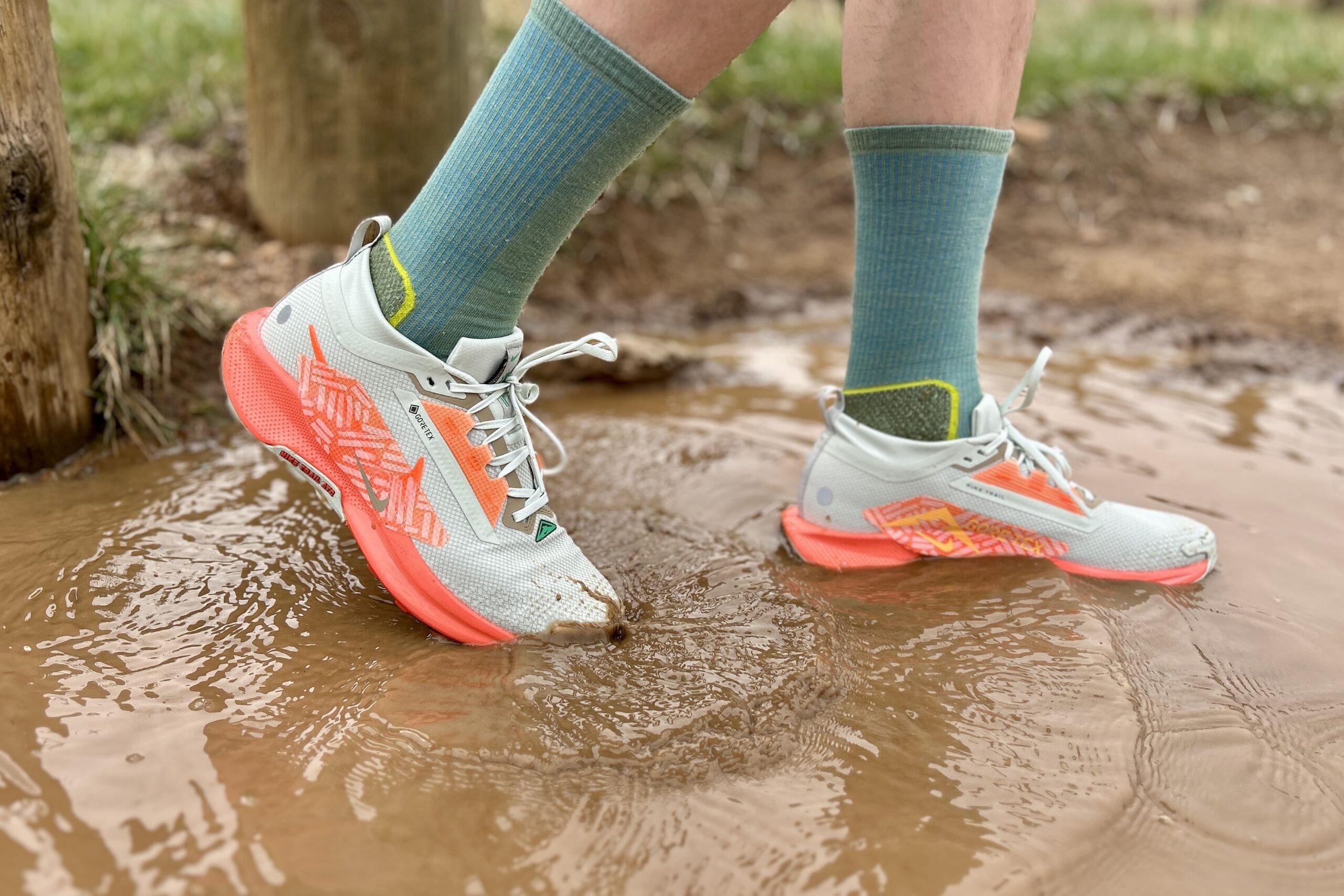 A person walks through a puddle of muddy water in a pair of white trail runners.