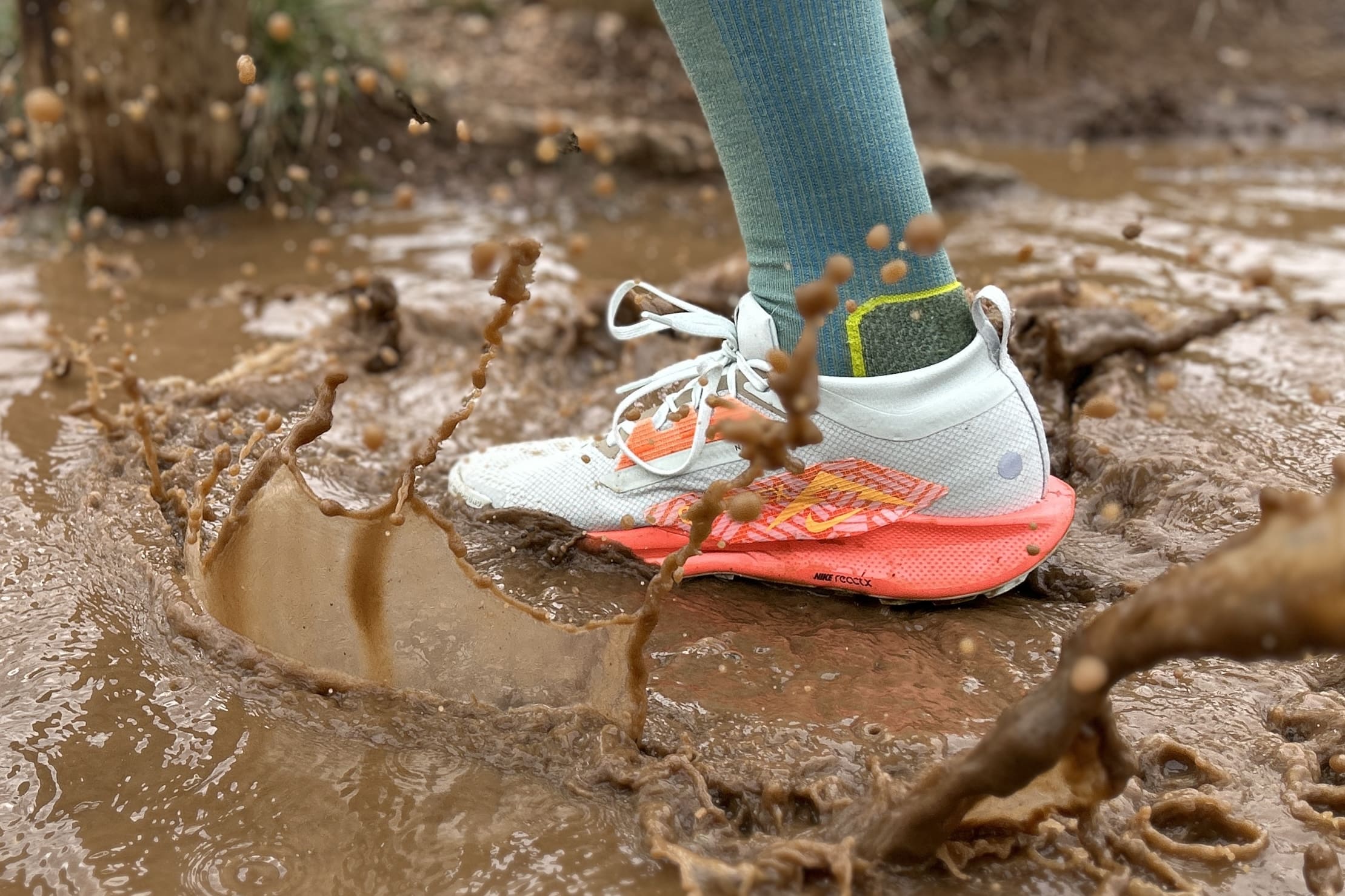 Close up of a person in running shoes splashing through a muddy puddle