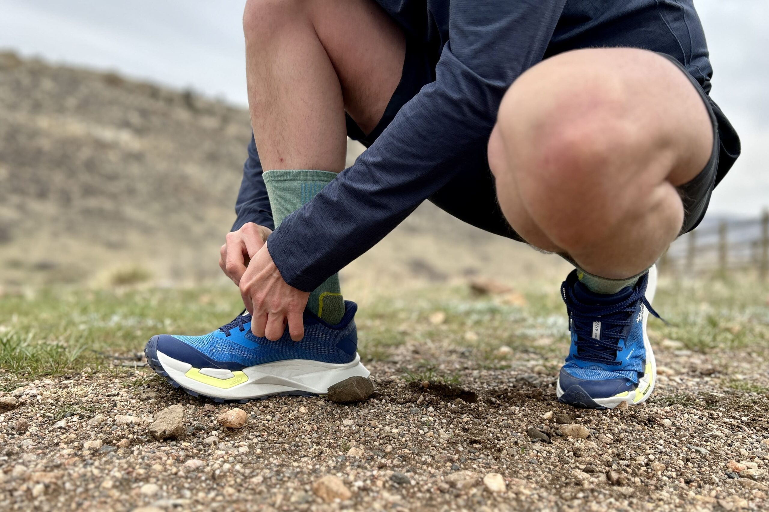 Close up image of a man from the waist down adjusting a pair of trail runners.