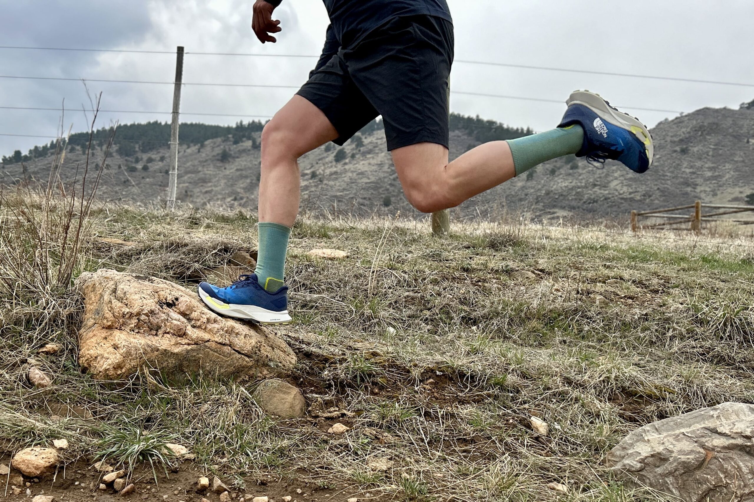 A person jumps onto a rock wearing shorts and trail runners, their back leg sticking up in the air.