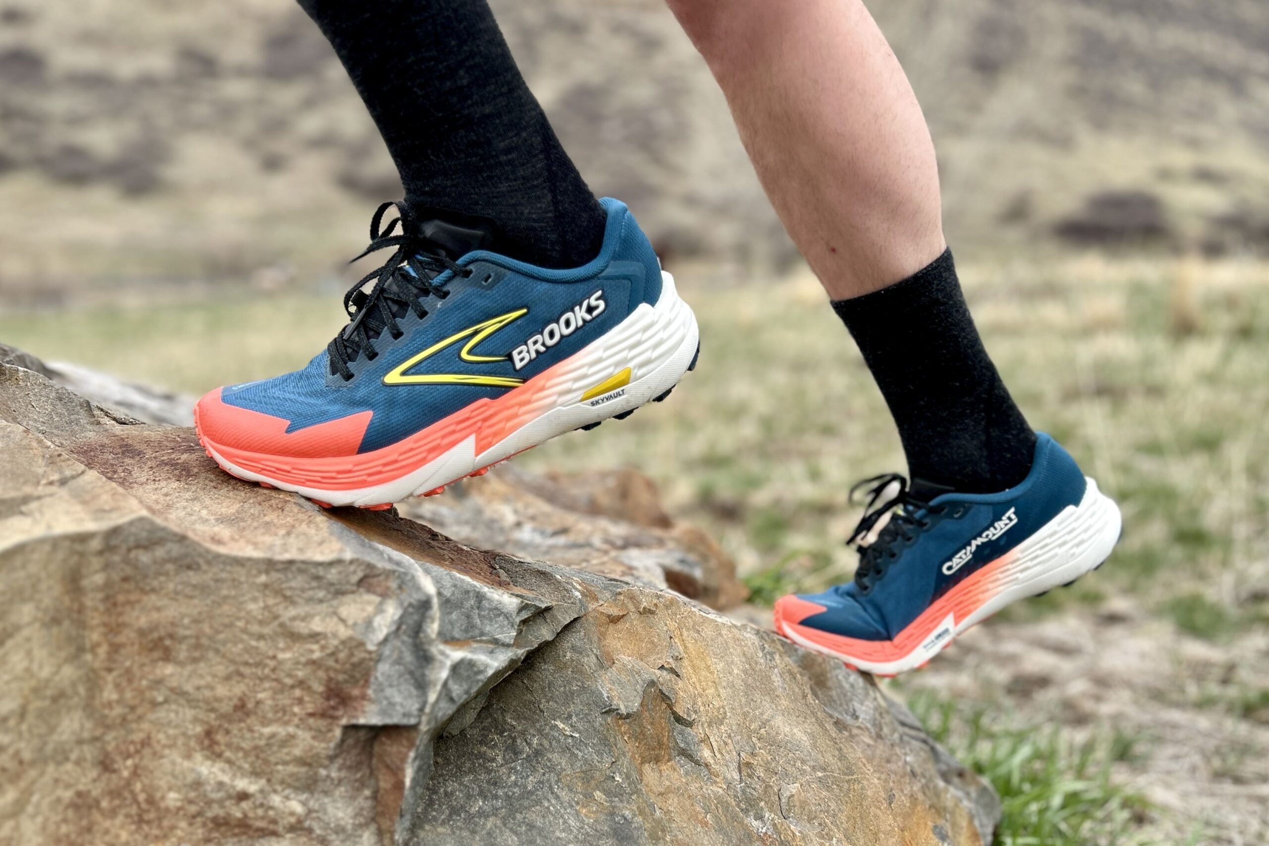 Close up image of a person ascending a steep rock in trail runners and tall socks.