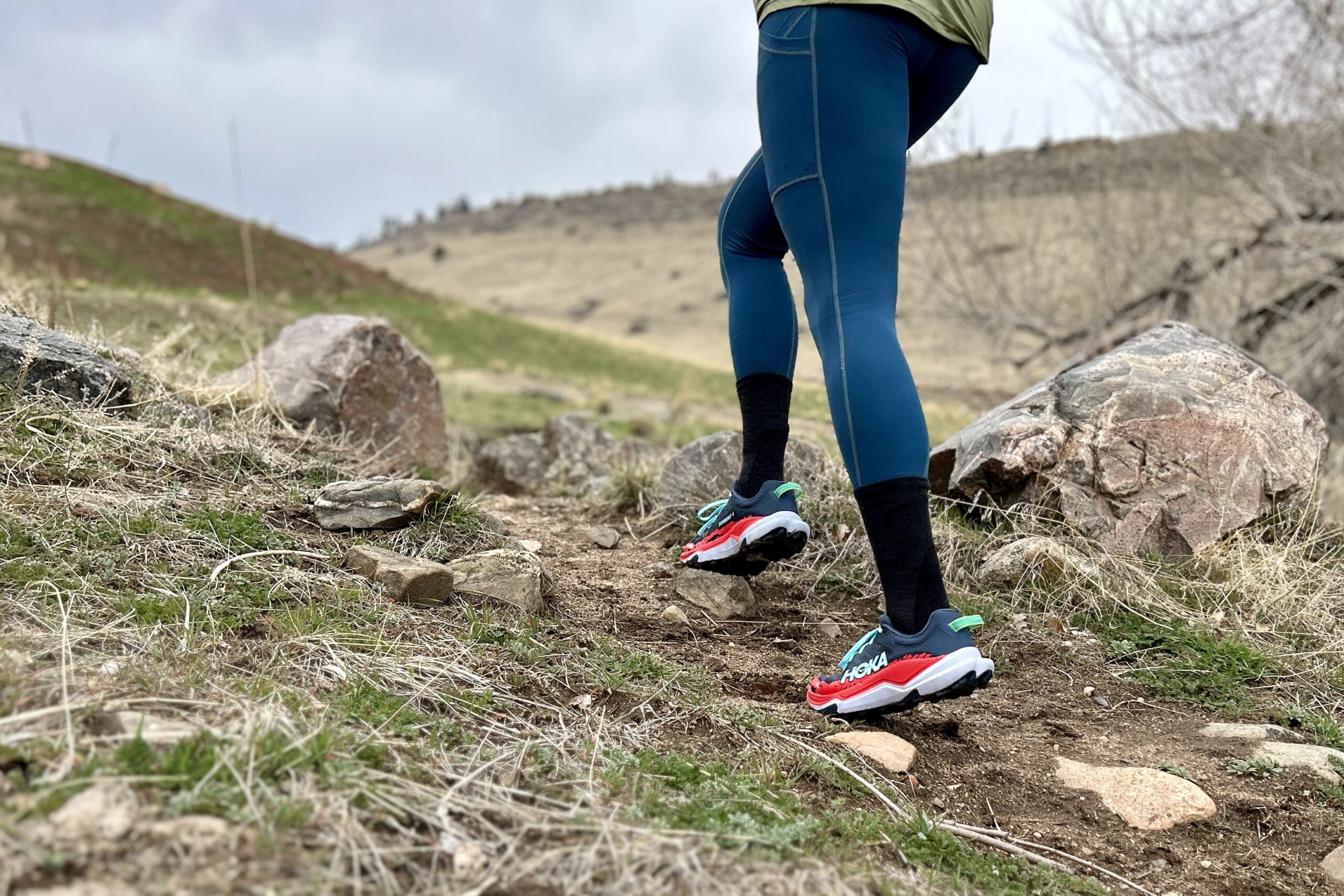A person running uphill in leggings and trail running shoes on a rocky trail.