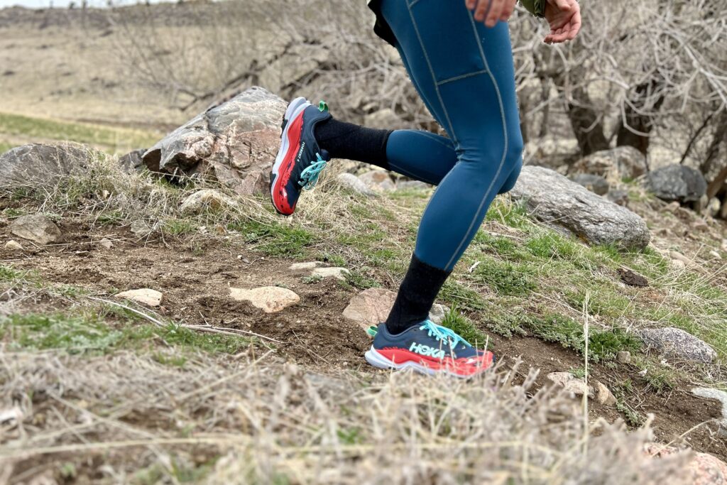 Image from the waist down of a person running uphill in leggings and trail running shoes on a rocky trail.
