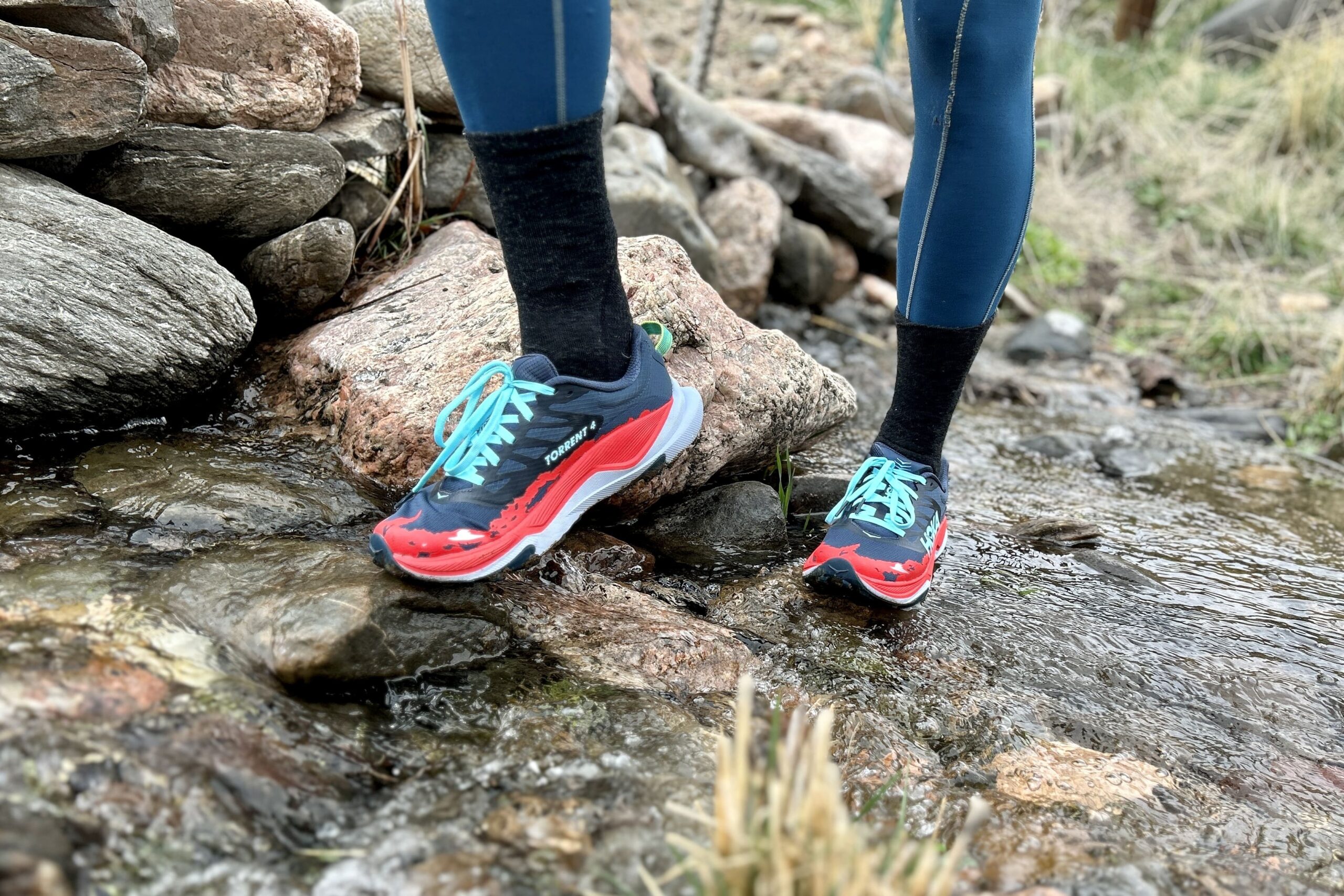 Close up from the knees down of a person in leggings and trail running sheos crossing a stream.