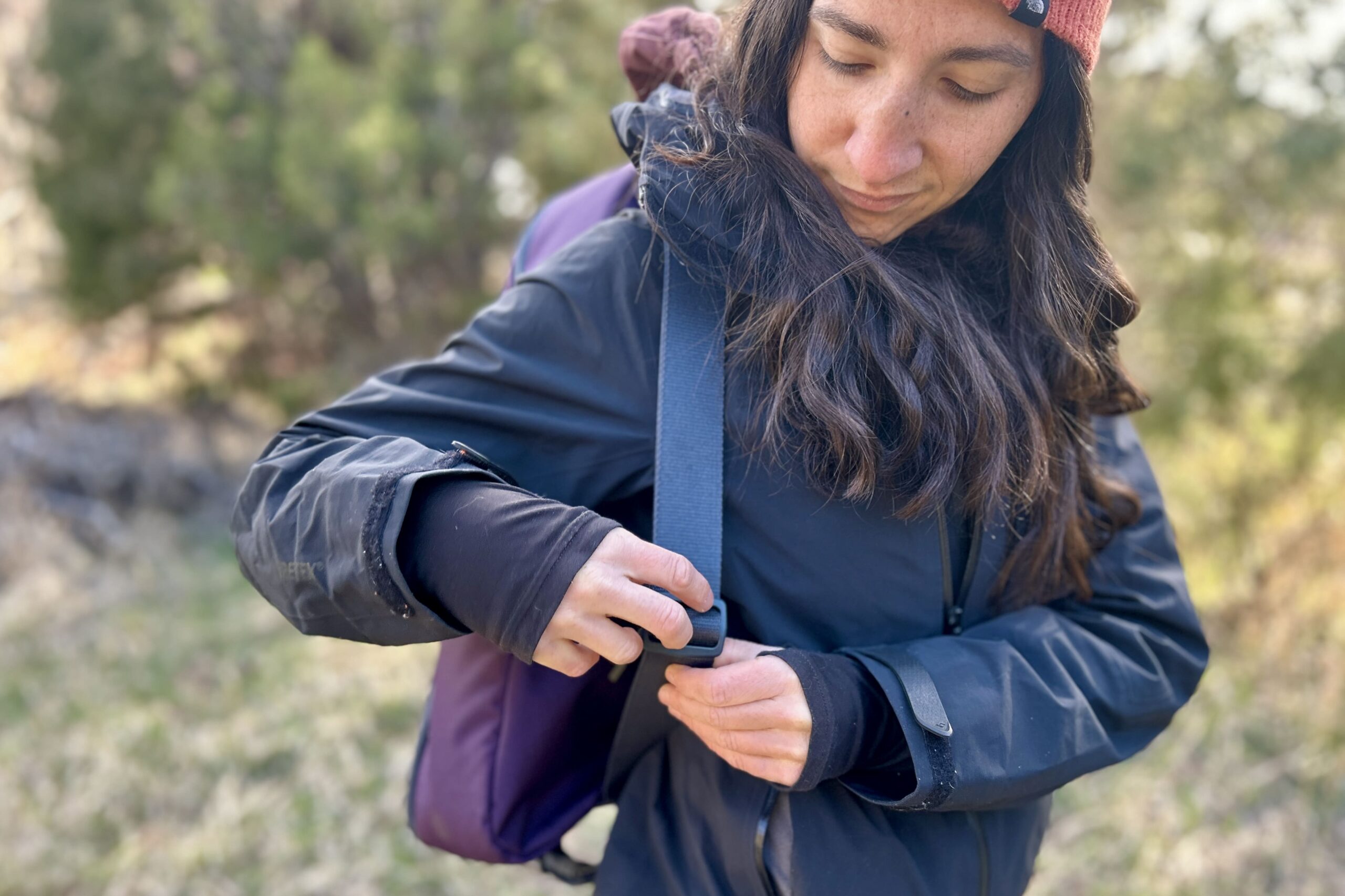 A woman wearing a camping chair case like a backpack adjusts the straps over her shoulders.