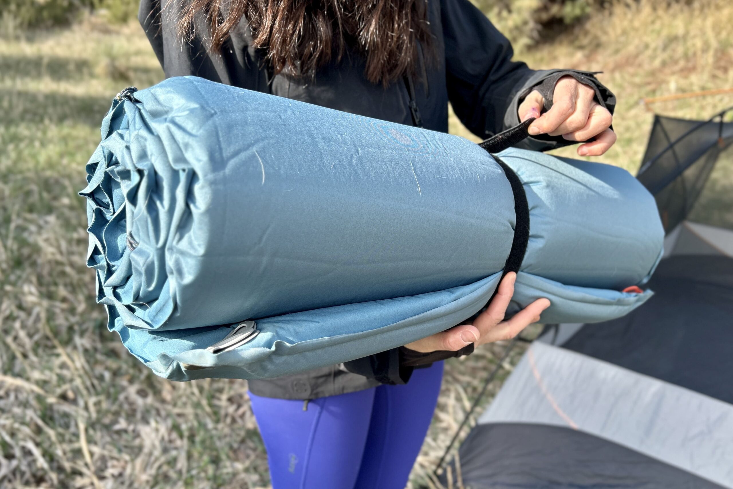 A woman puts a velcro tie around a camp mattress.