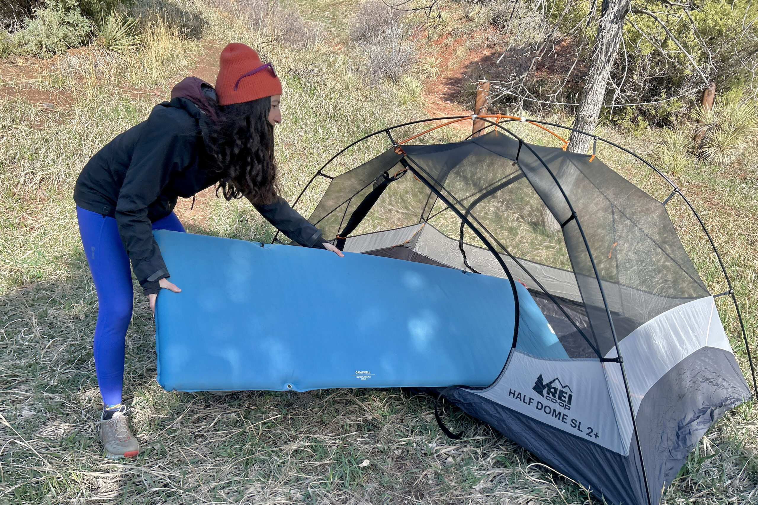 A woman puts a sleeping pad inside a tent in a wilderness setting.