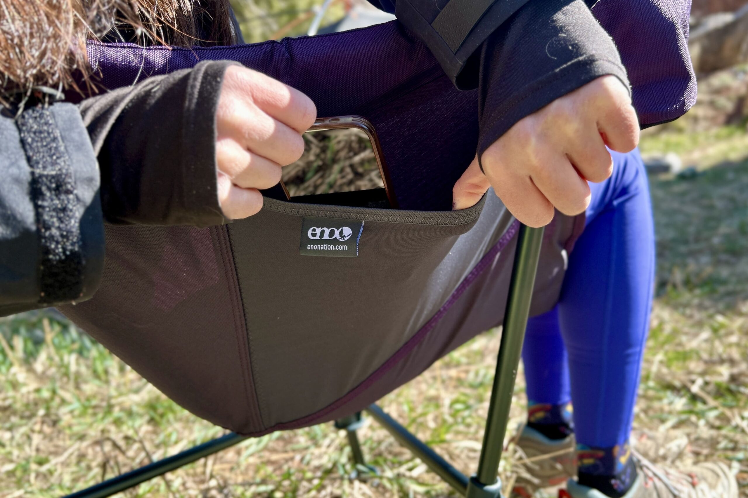 Close up image of a pocket on the side of a camping chair with someone pulling a phone out of it.