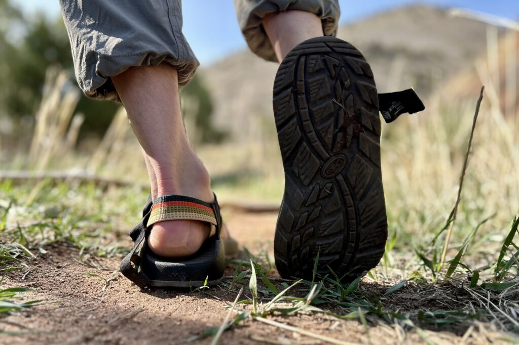 Close up image of a person walking in hiking sandals with one foot lifted and the traction visible.