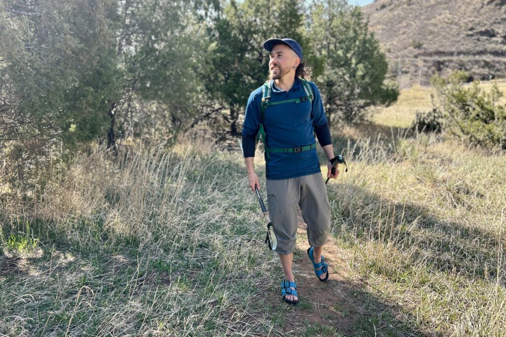 A man hikes through a forested setting in a backpack and sandals.