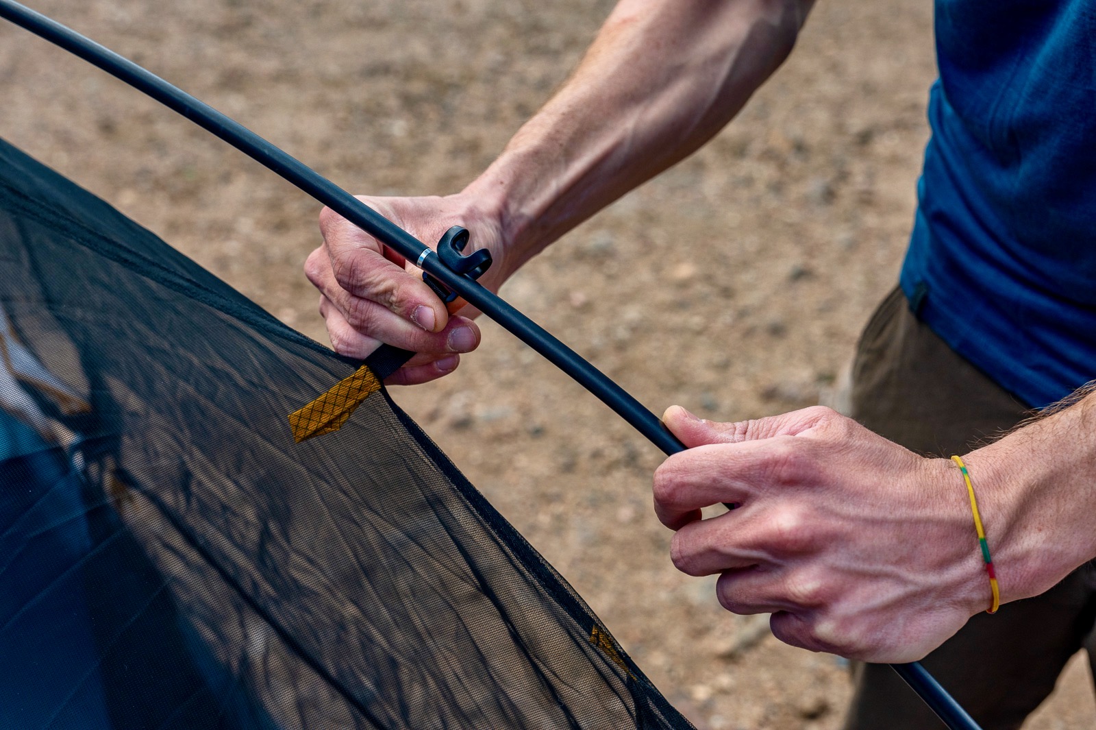 a close up of a hiker attaching the poles to a tent