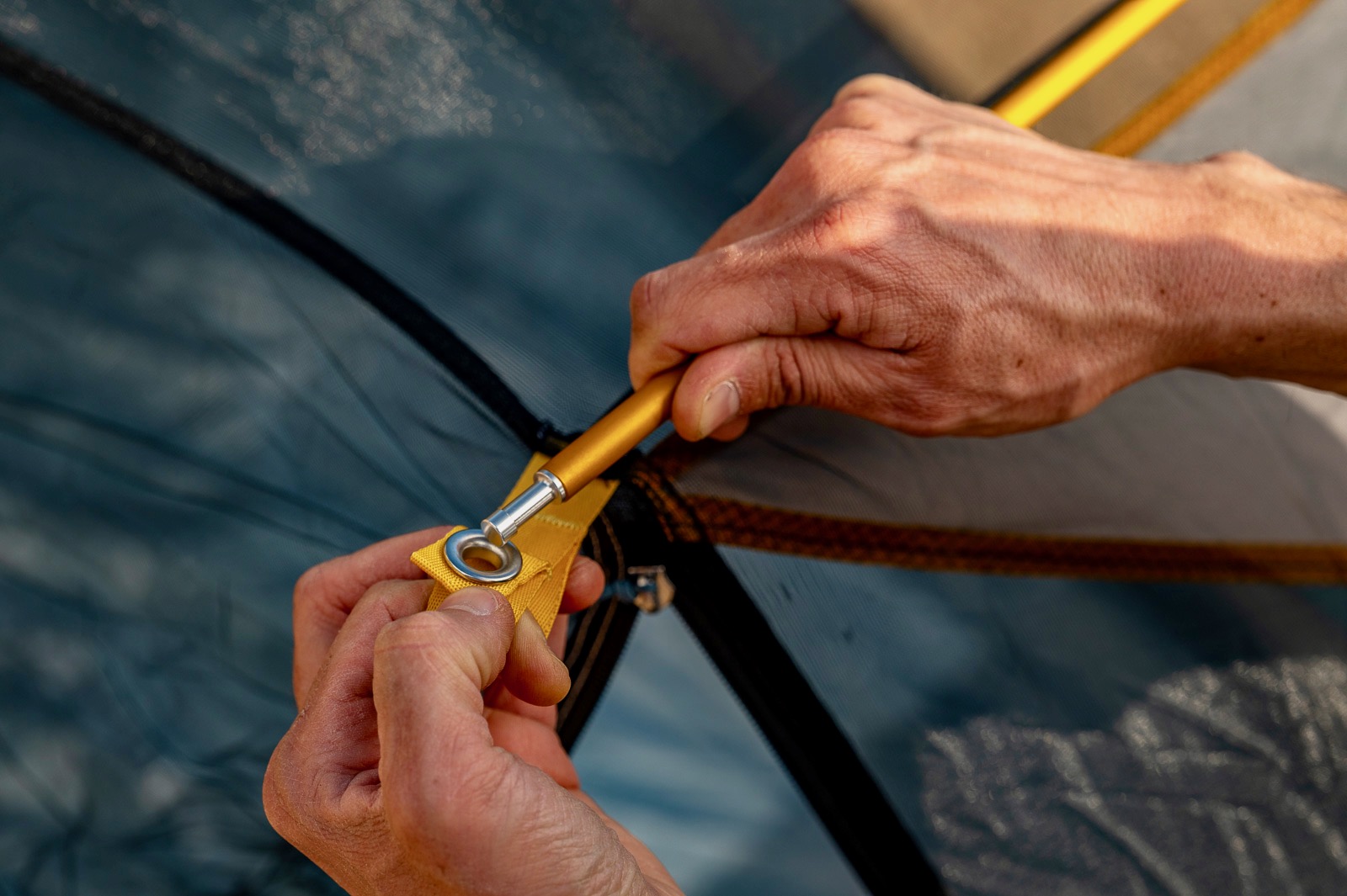 a close up of a hiker's hands attaching the poles to a tent