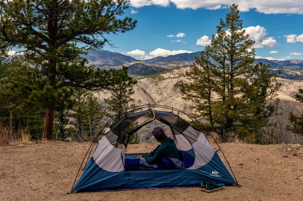a hiker sits in a tent without its rain fly, doors open, with a mountain view