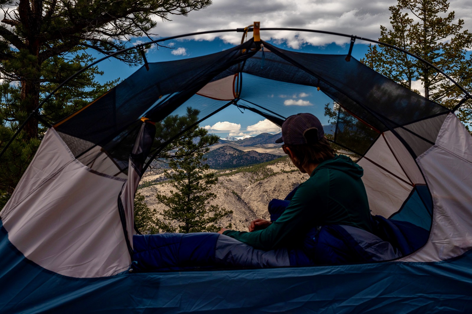 a hiker sits in a tent without its rain fly, doors open, with a mountain view