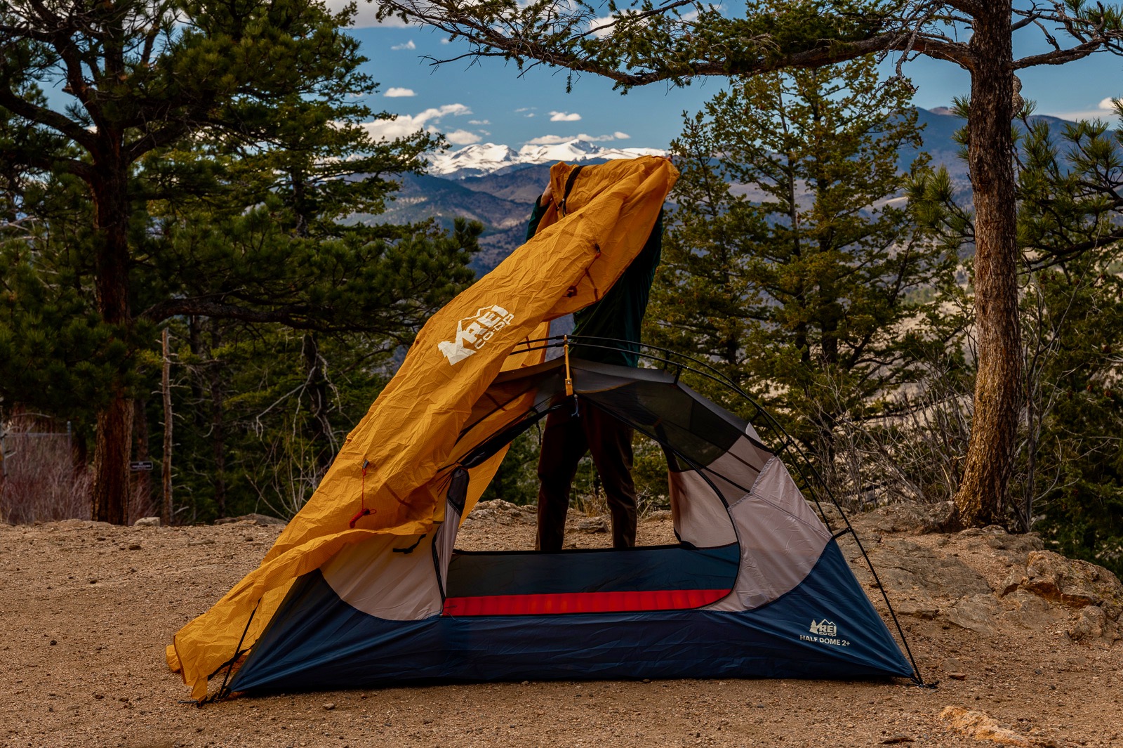 a hiker pulls a yellow rainfly over a tent