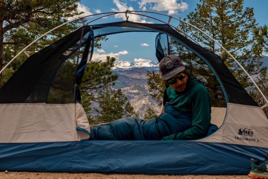 a hiker sits in a tent with no fly, doors open, and a mountain view