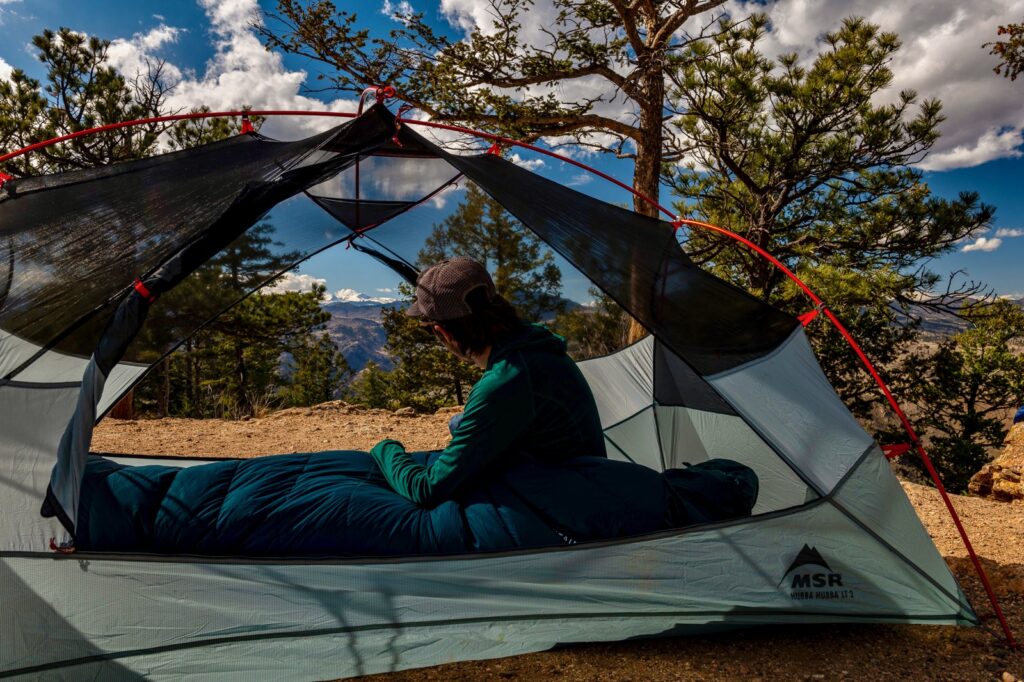 A hiker sits in a tent without the fly overlooking some mountains