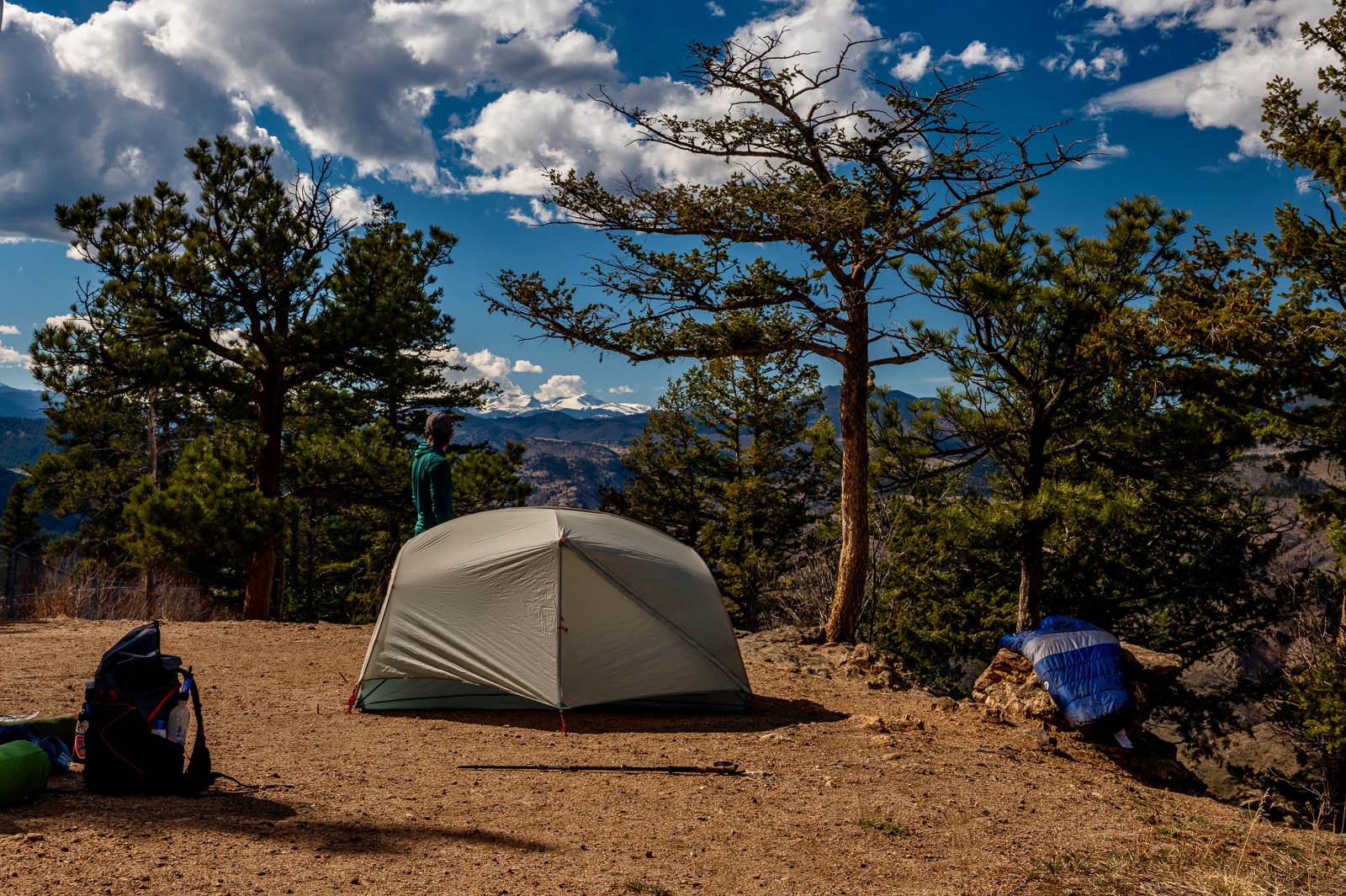 A hiker stands next to a tent looking off into the distance next to an msr tent and other gear sprawled nearby