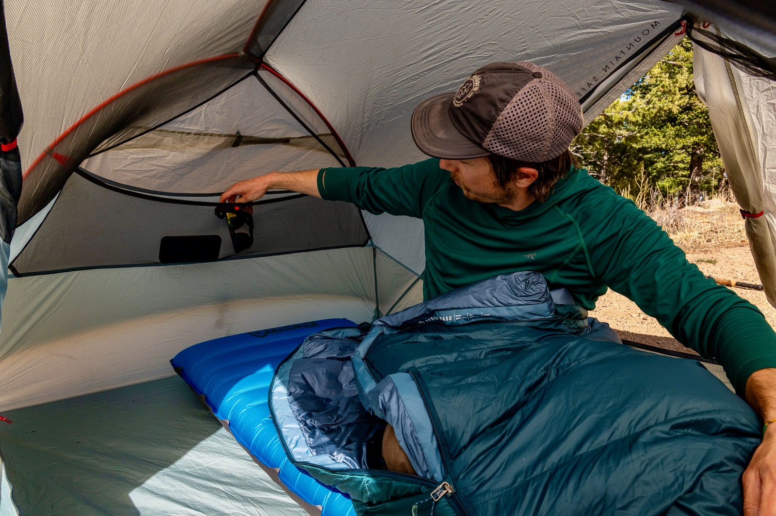 a hiker sits in a tent a reaches into a large mesh pocket behind him.