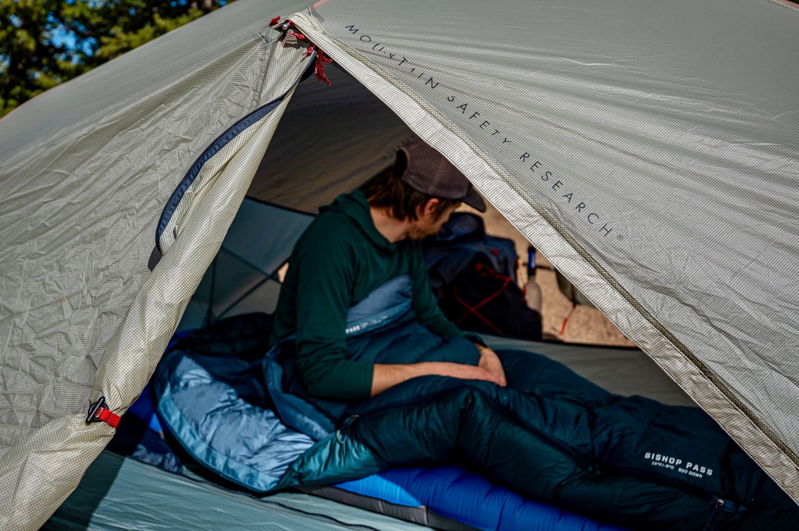 A hiker sits in a ten in a sleeping bag with the tent door in the foreground.