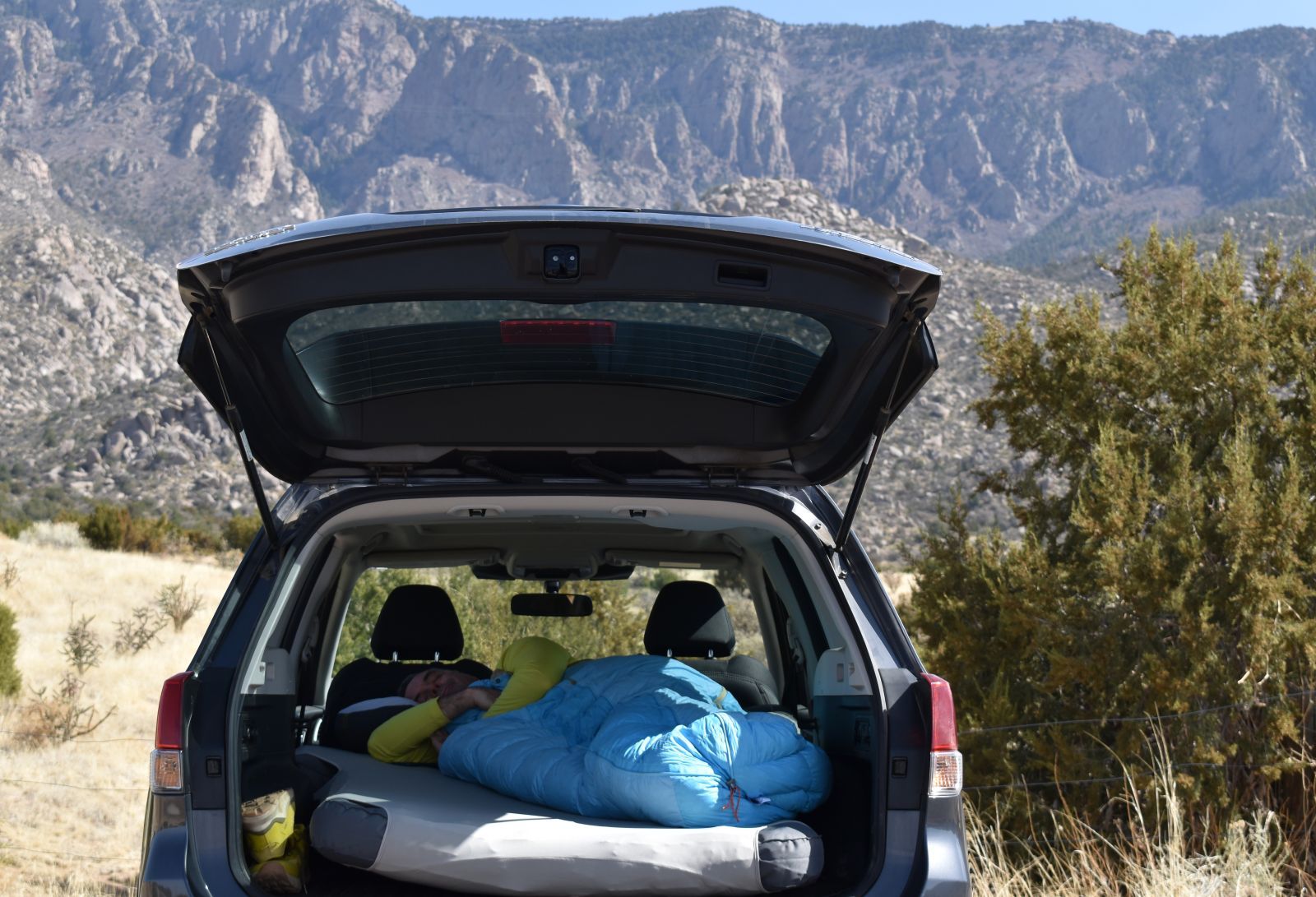 A camper sleeps on a custom vehicle air mattress with mountains in the background.