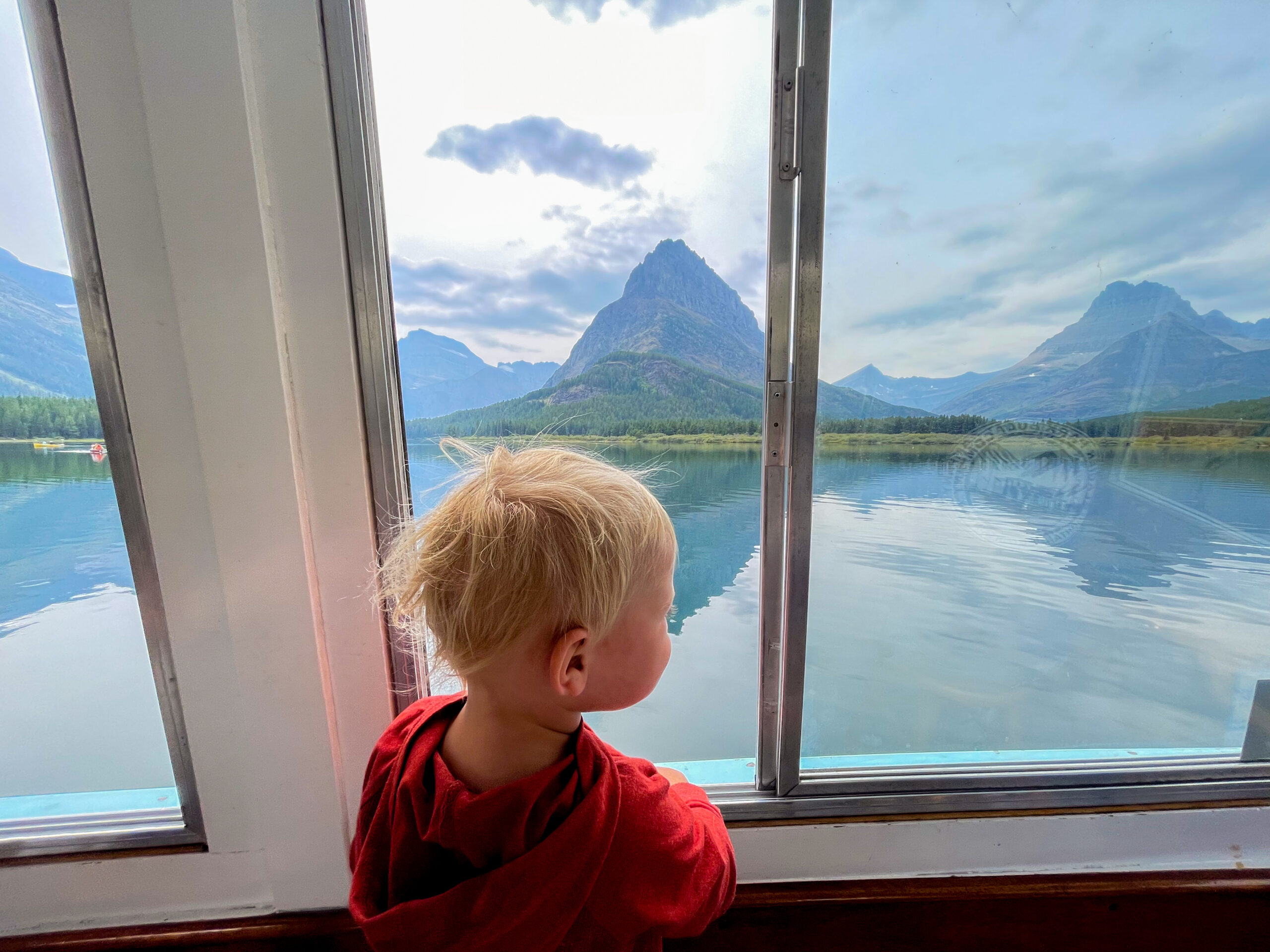 a little boy looks out a boat window at a mountina