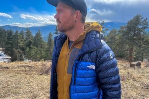 a man in a blue jacket standing in a field. He's facing somewhat away from the camera and lookign off into the distance.