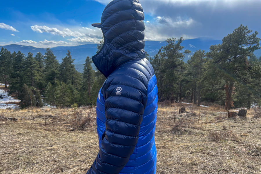 a man in a blue jacket standing in a field. He's facing away from the camera lookign at incoming rain clouds.