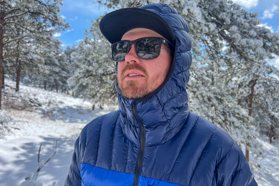 a man standing in a snowy forest. He's wearing a blue jacket looking off into the distance.