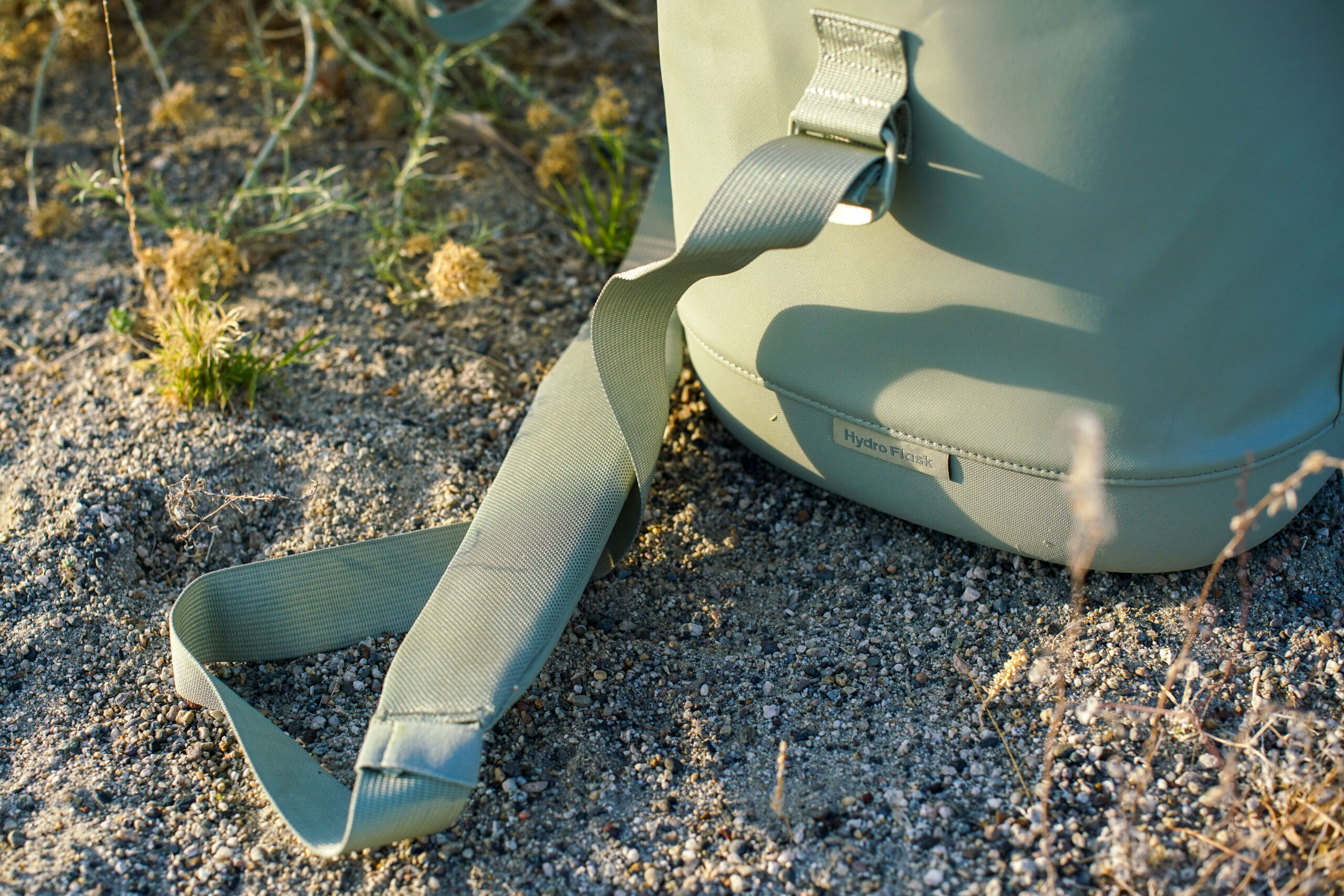 A close up of the shoulder strap on the Hydro Flask Carry Out 20L. The cooler and strap sit on the ground.
