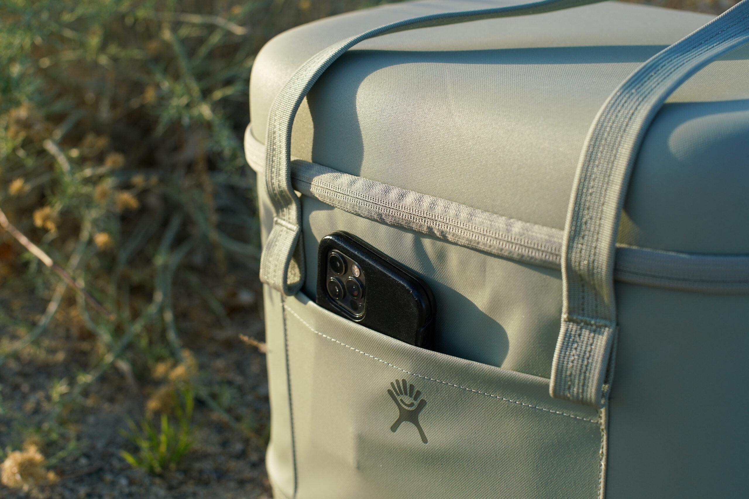 A close up of a cell phone poking out of the front pocket of the Hydro Flask Carry Out cooler.