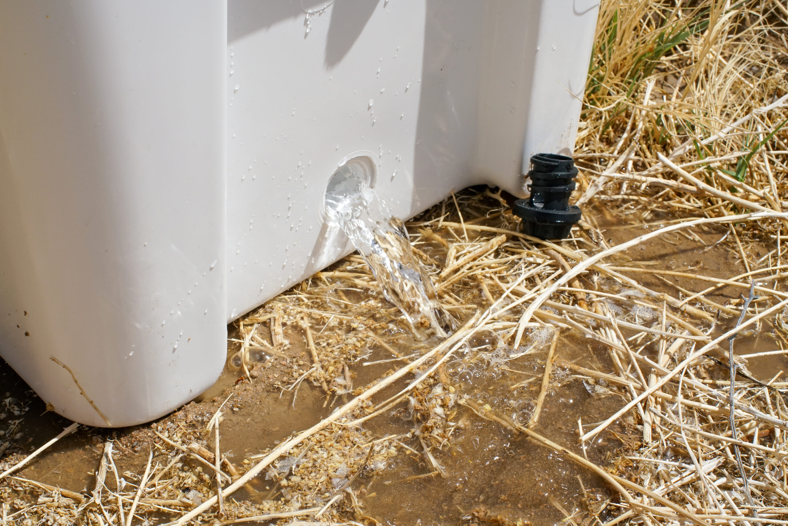 A close up of water pouring out a hole in the side of the YETI Tundra 65 cooler on to the ground.