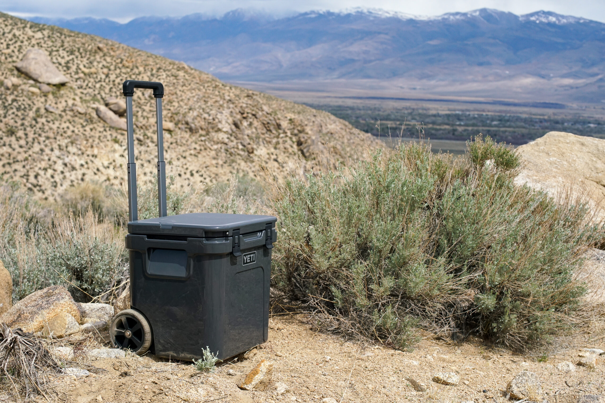 The YETI Roadie 48 cooler sits on the ground with mountains in the background.